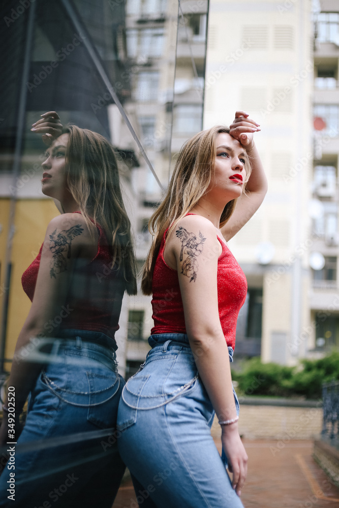 Young beautiful girl model posing in a red T-shirt and jeans on the background of a glass building. Street style,  fashion	
