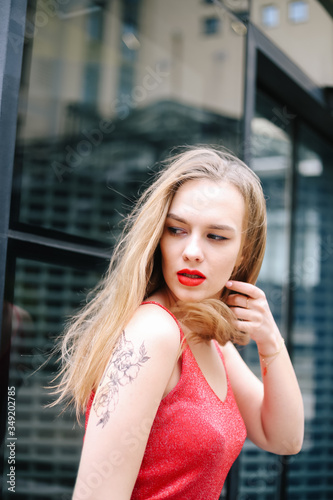 Young beautiful girl model posing in a red T-shirt and jeans on the background of a glass building. Street style, fashion 