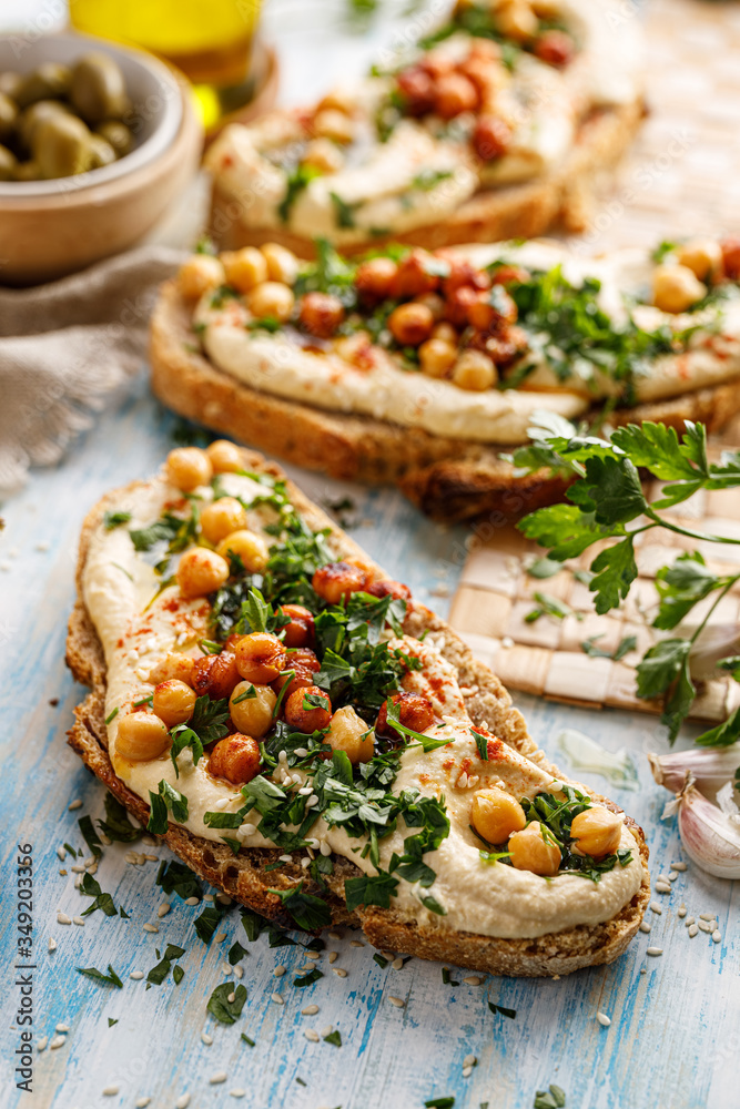 Vegetarian sandwich with addition hummus spread, fresh chopped parsley, chickpeas and olive oil close up view