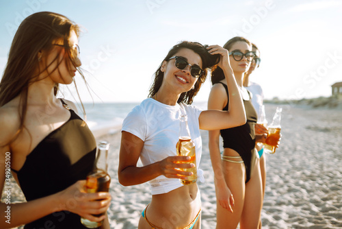 Young girls in bikinis having fun and drinking beer on beach. Girlfriends enjoying on beach holiday. Summer, relax and lifestyle concept.