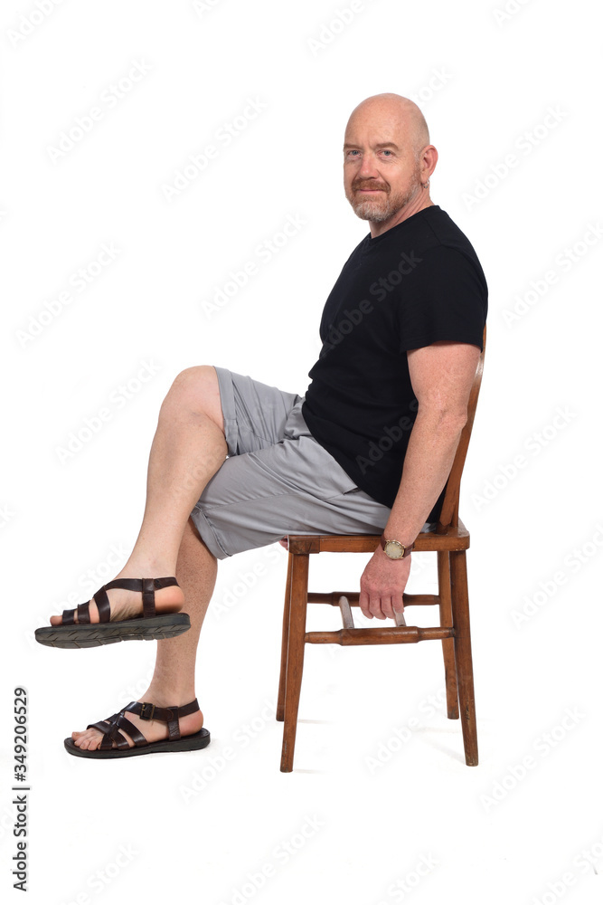 Bald man with sandals t-shirt and shorts sitting on white background, looking at camera Bald man with sandals t-shirt and shorts sitting on white background, looking at camera