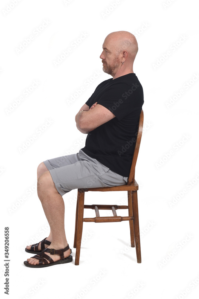 Bald man with sandals t-shirt and shorts sitting on white background, look side and arms crossed Bald man with sandals t-shirt and shorts sitting on white background, look side and arms crossed