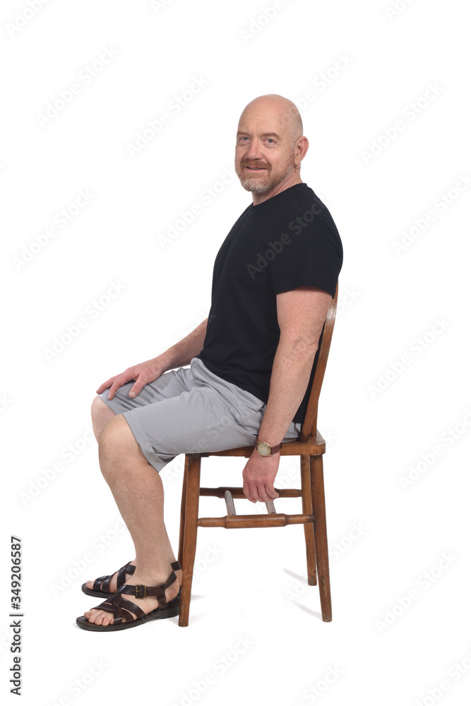 Bald man with sandals t-shirt and shorts sitting on white background, looking at camera