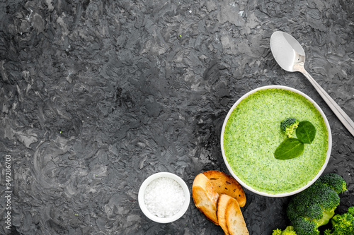 Broccoli cream soup, bread, spoon on grey kitchen desk top-down copy space