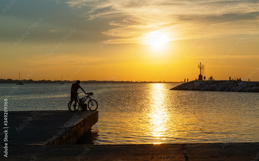 A man with a bicycle on the pier at sunset. Rimini, Italy.