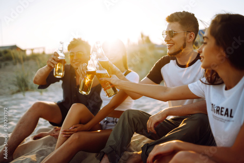 Group of young friends sitting together at the beach talking and drinking beers at sunset. Summer holidays, vacation, relax and lifestyle consept. © maxbelchenko