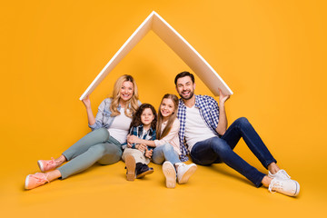 Photo offspring mommy daddy daughter small son happy together four member family support care hold hands roof above their head moving big dream house isolated yellow color background