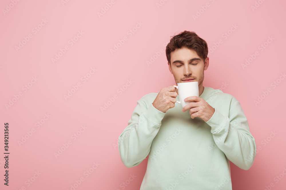 handsome young man enjoying flavor of coffee while holding white cup on pink background handsome young man enjoying flavor of coffee while holding white cup on pink background