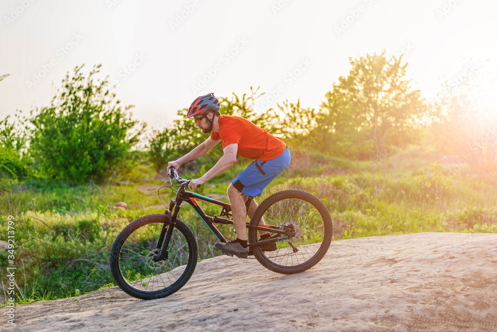 A cyclist in an orange T-shirt and helmet rides a mountain bike at sunset time.