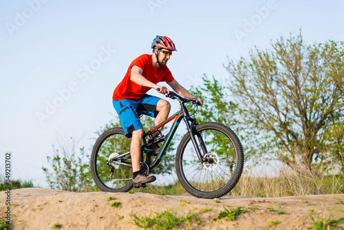 A cyclist in an orange T-shirt and helmet rides a mountain bike.