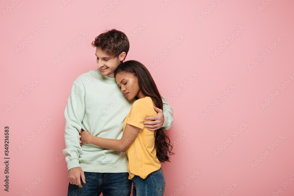 attractive african american girl with closed eyes and happy guy embracing on pink background attractive african american girl with closed eyes and happy guy embracing on pink background