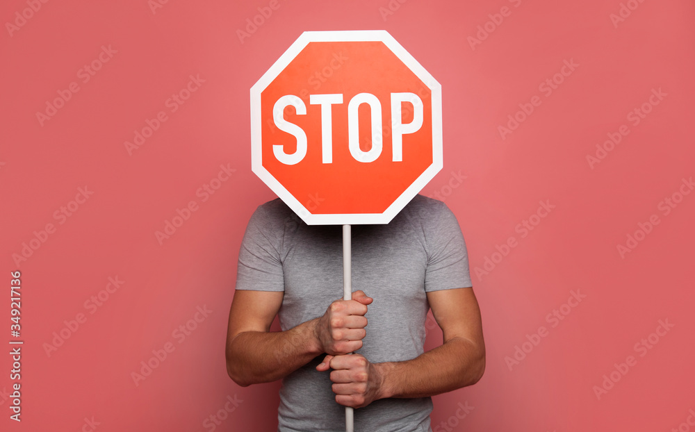 It's time to stop. Close-up photo of a young strong man, who is hiding behind a stop road sign, while holding it in his hands. - obrazy, fototapety, plakaty 