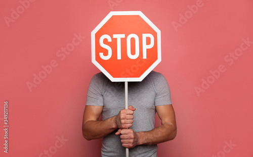 It's time to stop. Close-up photo of a young strong man, who is hiding behind a stop road sign, while holding it in his hands. photo