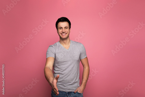 Nice to meet you. Close-up photo of a friendly young man in a casual clothes, who is smiling and stretching his arm to the camera, ready for a handshake.