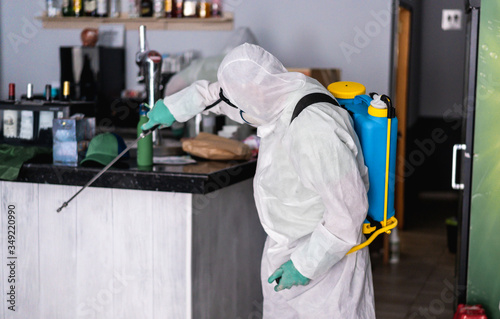 Worker in hazmat suit wearing face mask protection while making disinfection inside bar restaurant - Coronavirus decontamination for people healthcare - Focus on man's head