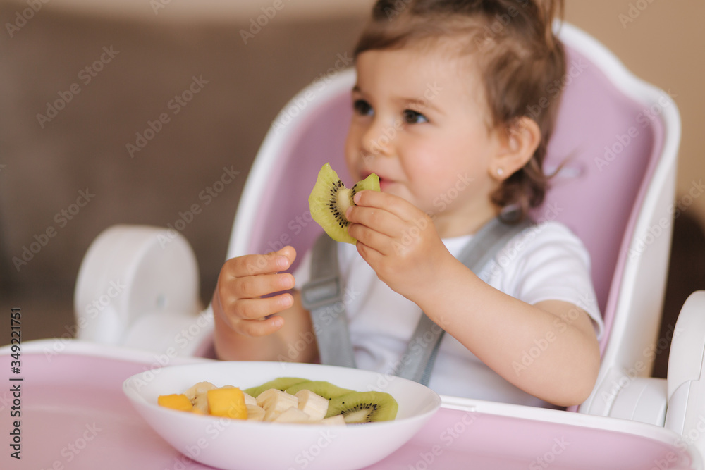Portrait of happy little kid eating kiwi in high chair. Healthy nutrition for kids Portrait of happy little kid eating kiwi in high chair. Healthy nutrition for kids