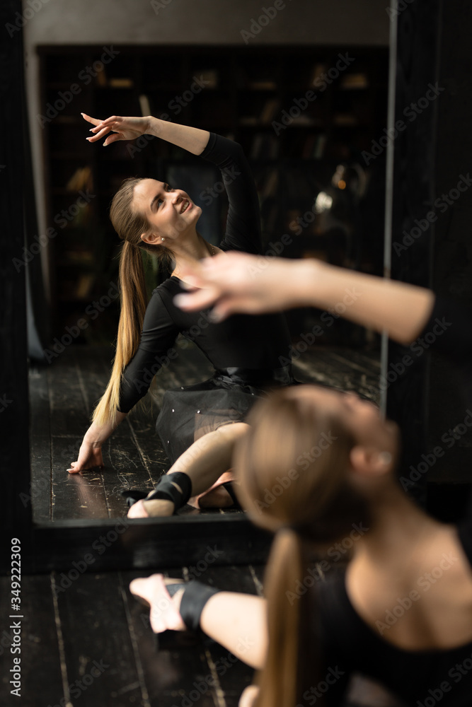 Fototapeta premium Reflection attractive ballerina practicing ballet in pointe shoes, sitting in front of a black mirror.