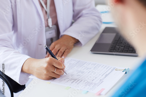 Close-up of doctor sitting at the table and filling the form he prescribing a medicine for patient