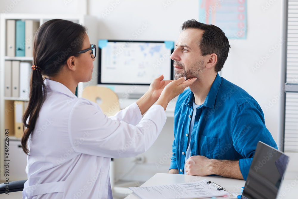 Female doctor examining the patient's throat while he sitting at the hospital during his visit Female doctor examining the patient's throat while he sitting at the hospital during his visit
