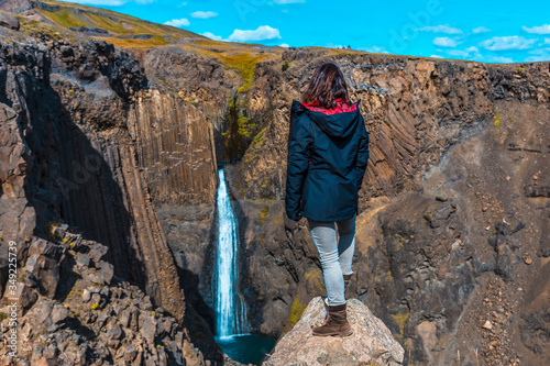 A young woman looking at the waterfall above Hengifoss from above. Iceland photo