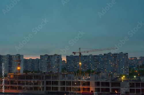 Two construction cranes over standing buildings at night. continuous infrastructure construction