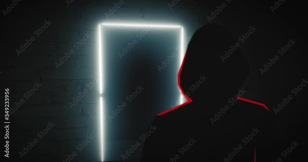 Silhouette person with a hood stands in front of a spiritual glowing door frame. Reveal shot. Silhouette person with a hood stands in front of a spiritual glowing door frame. Reveal shot.