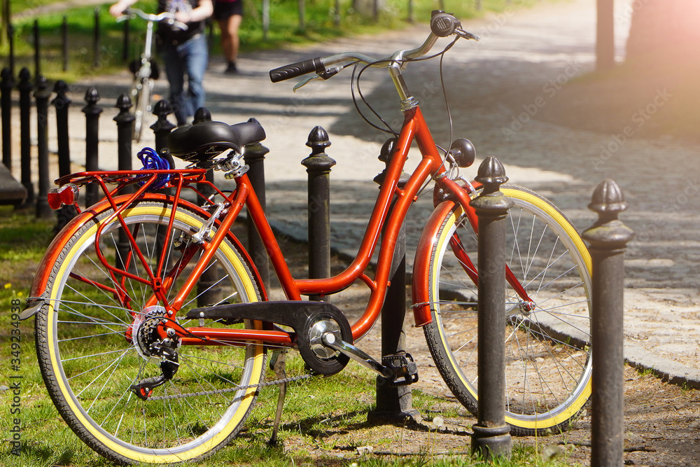 A bright red Bicycle stands at the fence in a green Park on a Sunny day. Moving by bike every day. bicycle at street parking outdoors. use of eco-friendly and sports transport in the city to move