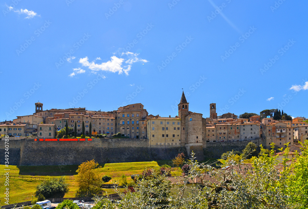 landscape with Anghiari italian medieval village city walls on green hill and blue sky in background. Arezzo, Tuscany Italy Europe.