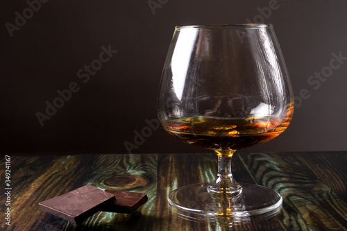 Glass with cognac and dark chocolate. Dear elite alcohol on a dark brown background. Alcoholic drinks.