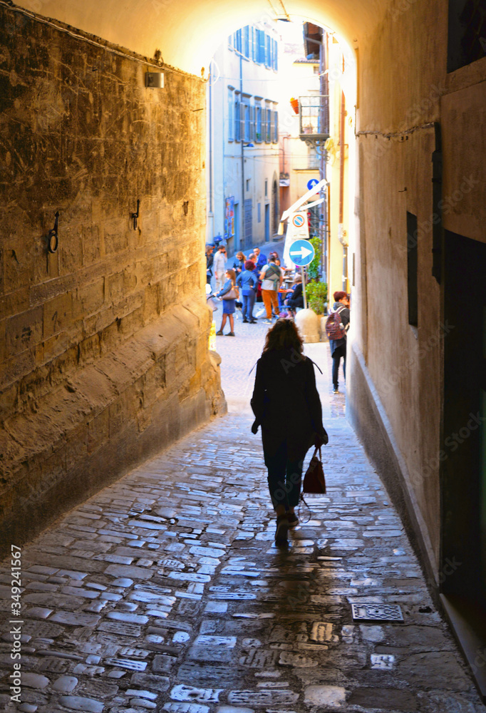 Woman walks in narrow street near Corso Cavour street with people in old historic center in medieval town Citta di Castello near Perugia in Umbria, Italy
