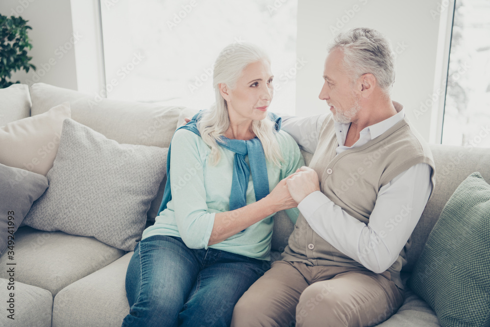 Photo of two pretty aged people pair holding arms emotionally look eyes sitting cozy sofa indoors