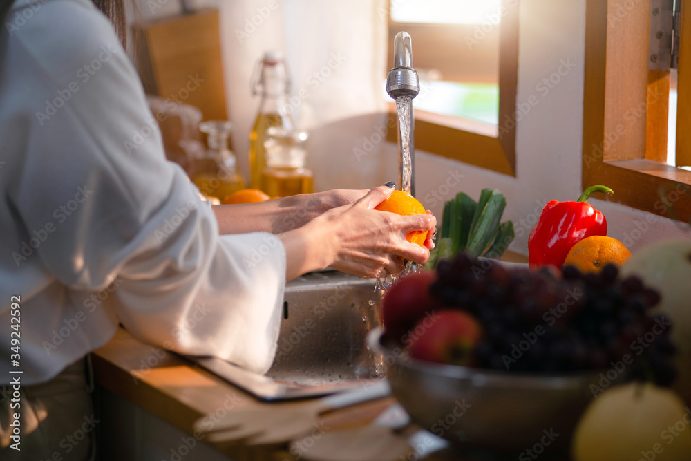 Healthy Asian woman washing fruit above kitchen sink, pouring water on woman hands and fruit Healthy Asian woman washing fruit above kitchen sink, pouring water on woman hands and fruit