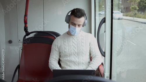 A man in a mask works with the computer while traveling on a public transport urban bus