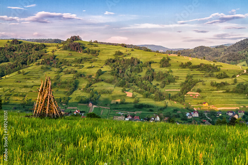 Fototapeta Naklejka Na Ścianę i Meble -  Traditional Slovenian constructions for drying hay and wood storage, hayrack on the hilly field in Beskid Sadecki mountains, Poland. Lomnica Zdroj and Piwniczna towns in the background.