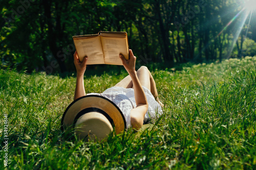 girl in the hat reading a book lying in meadow grass