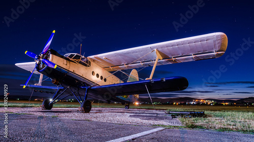 Old vintage classic airplane on small airfield in night time with clear sky. Abandoned biplane in long exposure under the stars