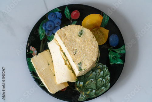 a piece of homemade cheese with dill and spices on a black plate