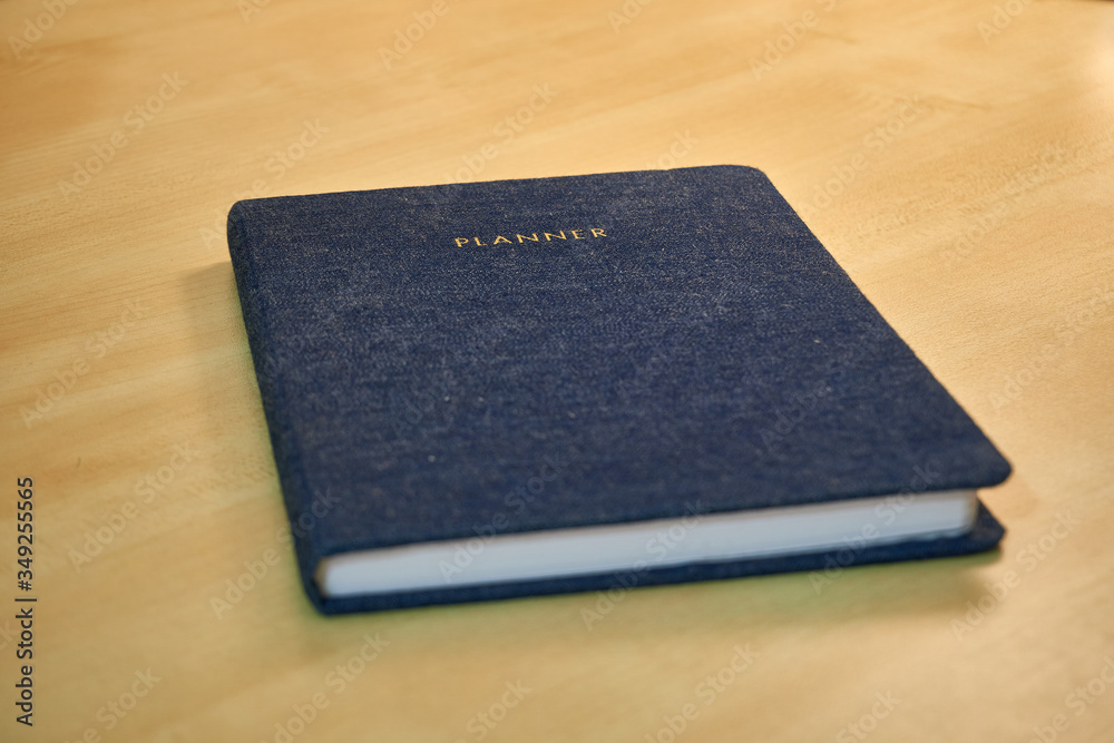 Planner or organizer notebook with jeans texture material cover, a diary to make appointment meeting or manage timetable close book on a wooden office desk Planner or organizer notebook with jeans texture material cover, a diary to make appointment meeting or manage timetable close book on a wooden office desk