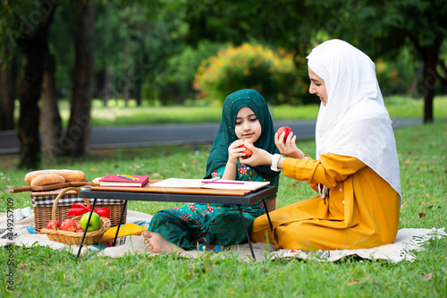 Happy Asian family Arabic Muslim mother and little girl child with hijab dress smiling, talking, learning apportion and having fun moment good time in park. Happy Muslim family mom and child concept. © Songpon