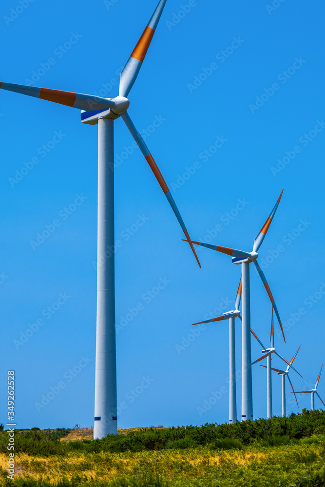 A row of three-bladed wind farms on an Alpine meadow against a blue sky. Copy space. A row of three-bladed wind farms on an Alpine meadow against a blue sky. Copy space.