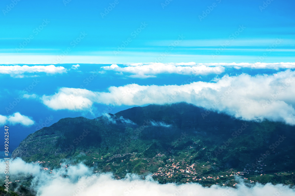 A picturesque mountain landscape with the top of a mountain range above white clouds. On the slope of the mountain there are villages with developed infrastructure. The view from the top. Copy space.