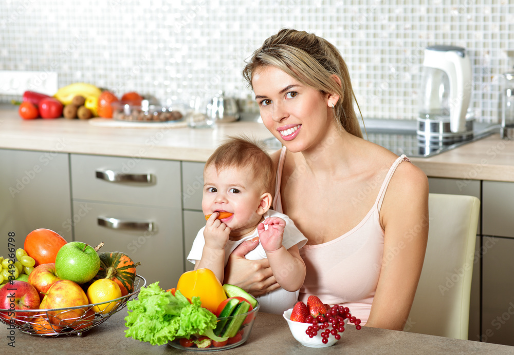 Happy young mother with a baby in the kitchen interior. Fresh vegetables and fruits.