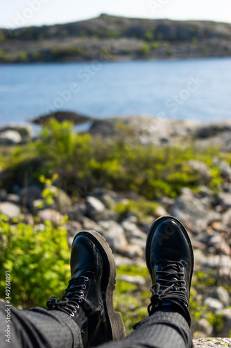 Photo of two black elegant boots sitting on the nature contemplating a green landscape next to the sea.