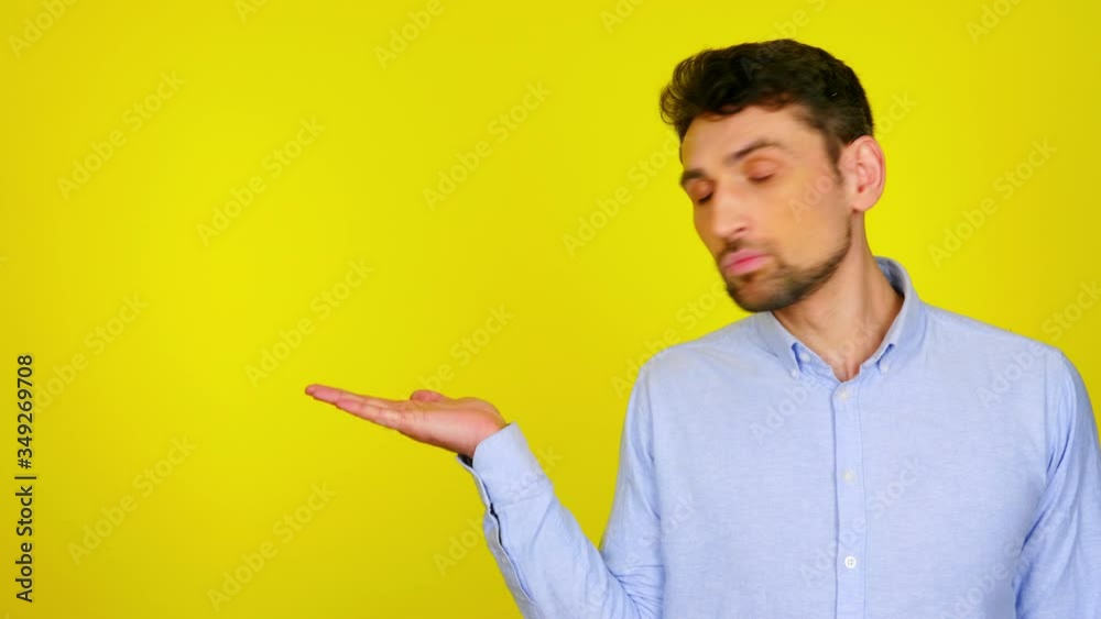 Handsome bearded man in a light blue shirt demonstrates an imaginary product in the palm of his hand. The guy on a yellow background shows with his hand a possible product or text Handsome bearded man in a light blue shirt demonstrates an imaginary product in the palm of his hand. The guy on a yellow background shows with his hand a possible product or text