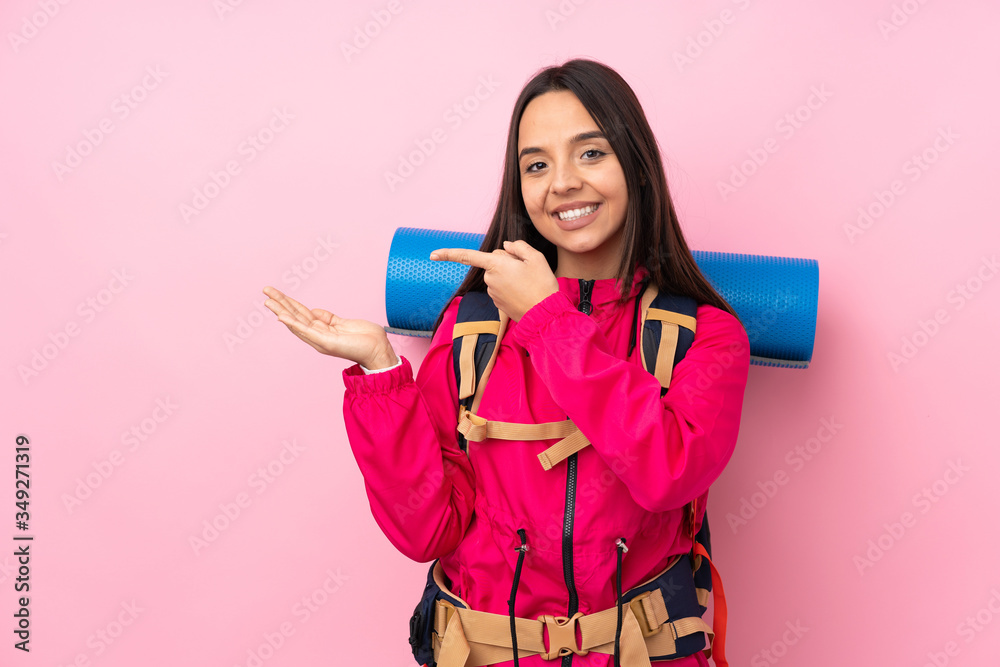 Young mountaineer girl with a big backpack over isolated pink background holding copyspace imaginary on the palm to insert an ad Young mountaineer girl with a big backpack over isolated pink background holding copyspace imaginary on the palm to insert an ad