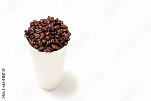 a large cardboard Cup filled with roasted brown coffee beans. the glass is located on a white empty background on the left side of the frame. coffee background for ads  menus or promotions