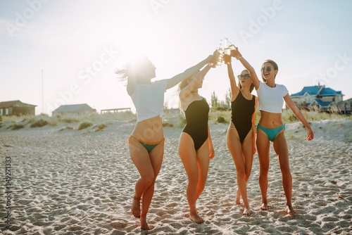 Happy Four girls walking and drinking beers on the beach at sunset. Young women enjoying on beach holiday.  Summer holidays, vacation, relax and lifestyle concept.