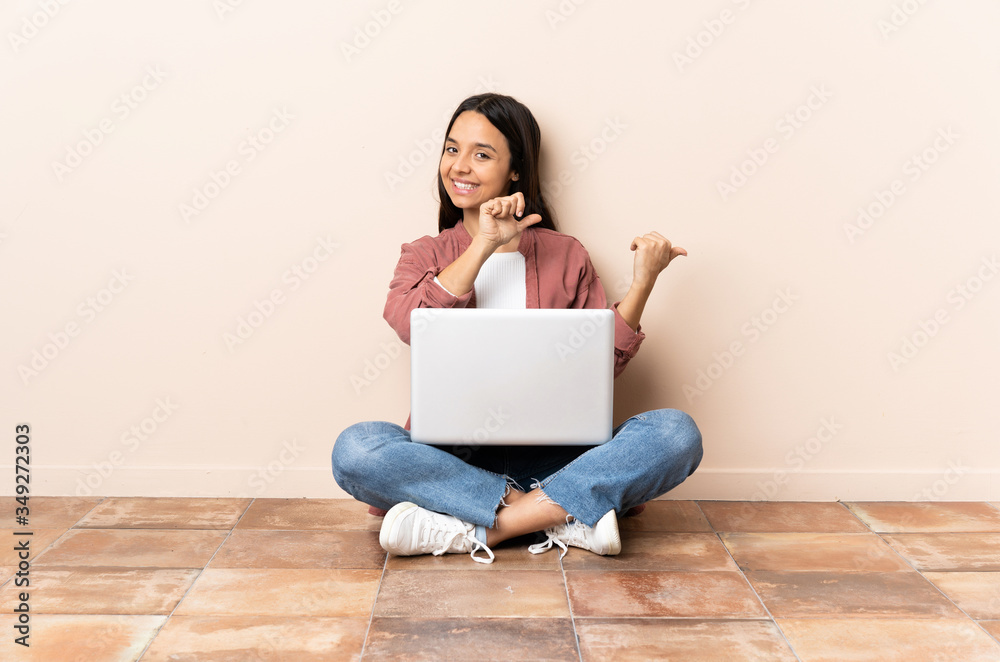 Young mixed race woman with a laptop sitting on the floor pointing to the side to present a product Young mixed race woman with a laptop sitting on the floor pointing to the side to present a product