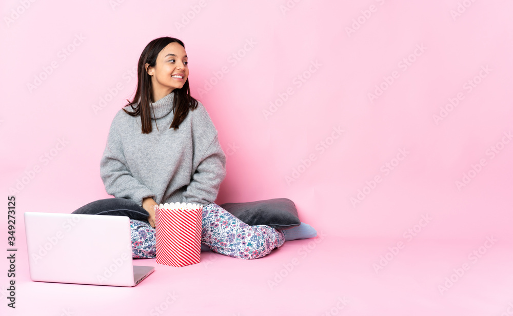 Young mixed race woman eating popcorn while watching a movie on the laptop in back position and looking side Young mixed race woman eating popcorn while watching a movie on the laptop in back position and looking side