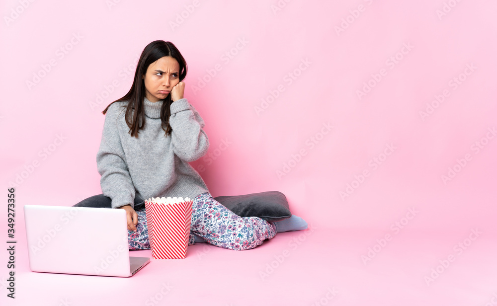 Young mixed race woman eating popcorn while watching a movie on the laptop with tired and bored expression Young mixed race woman eating popcorn while watching a movie on the laptop with tired and bored expression